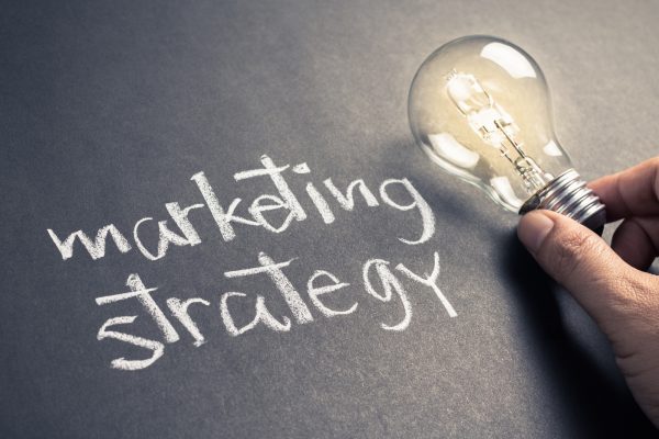 Handwriting-of-Marketing-Strategy-text-on-chalkboard-with-glowing-light-bulb